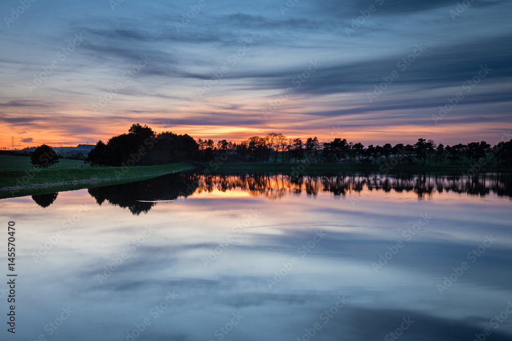 Obraz premium Zmierzch w Whittle Dene Reservoir / Whittle Dene Reservoir w Northumberland to popularne miejsce do wędkowania, widziane tutaj o zmierzchu, odbijające niebo
