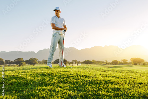 Male golfer with golf club on field looking away