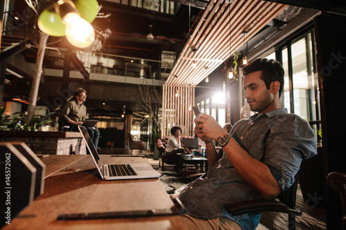 Handsome young man sitting at office cafe using phone