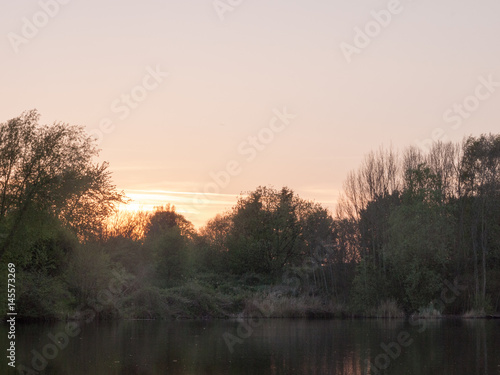 a beautiful sunset over a lake with trees and reeds
