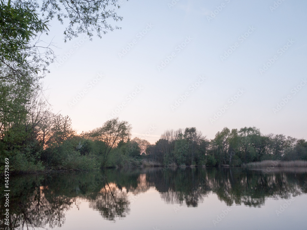 Obraz premium sunsetting over a lake as the trees around are reflected in the water