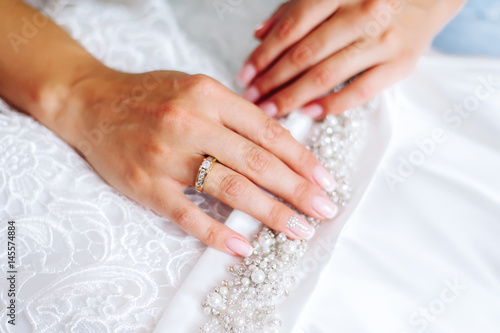 Hand of the bride with a ring on a white dress.