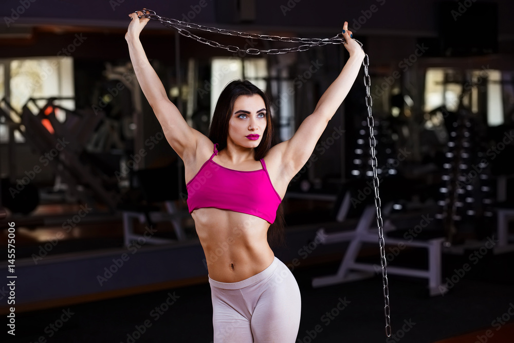 Attractive young muscular woman bodybuilder with perfect body posing with chain in gym Attractive young muscular woman bodybuilder with perfect body posing with chain in gym