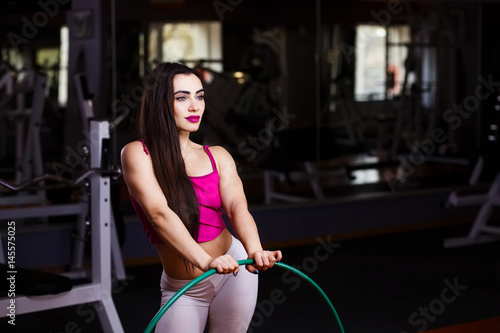 Young attractive young muscular woman bodybuilder with perfect body posing with hula hoop in gym