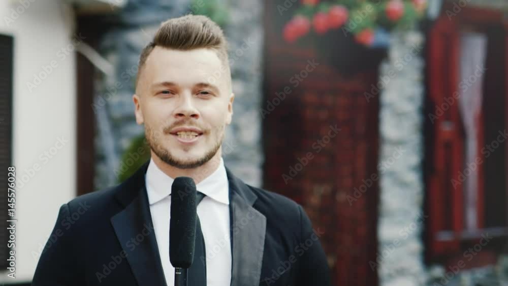 An elegant, bold-looking man speaks into the microphone. It stands and looks into the camera - the leader of the holidays or the TV host An elegant, bold-looking man speaks into the microphone. It stands and looks into the camera - the leader of the holidays or the TV host