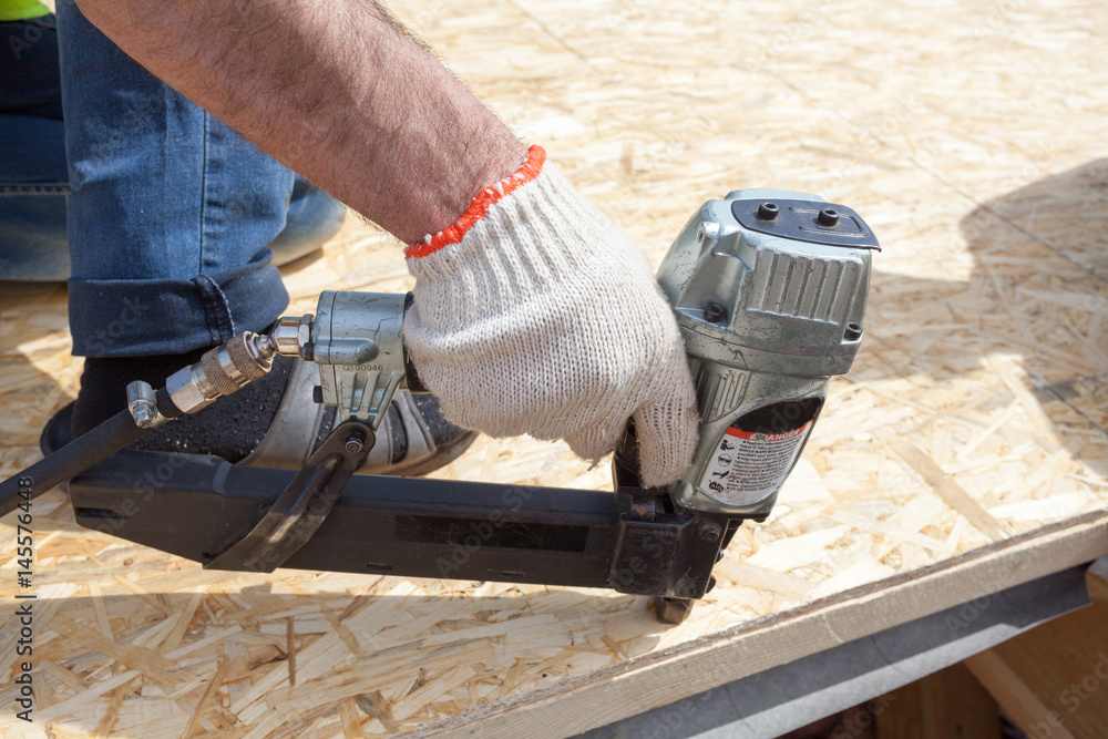 Construction worker using nail gun to nail Oriented Strand Board osb sheeting on roof of a new home Construction worker using nail gun to nail Oriented Strand Board osb sheeting on roof of a new home