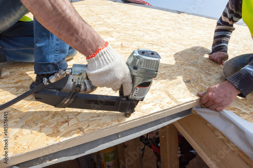 Construction worker using nail gun to nail Oriented Strand Board osb sheeting on roof of a new home