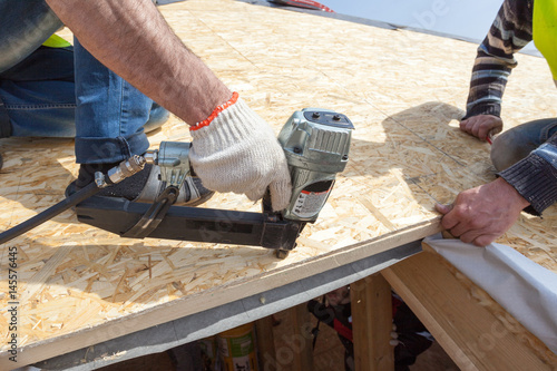 Construction worker using nail gun to nail Oriented Strand Board osb sheeting on roof of a new home photo
