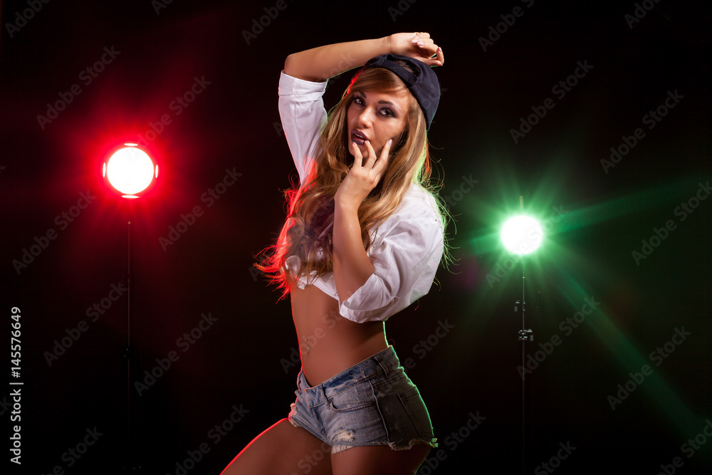 Hot sexy woman in white shirt with two lights from behind in studio photo on black background