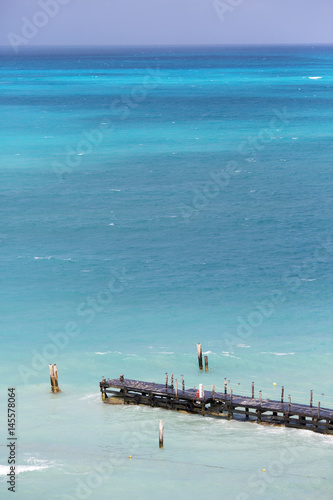 Aerial view to the sea. Long wooden pier in front. Focus point on the dock.