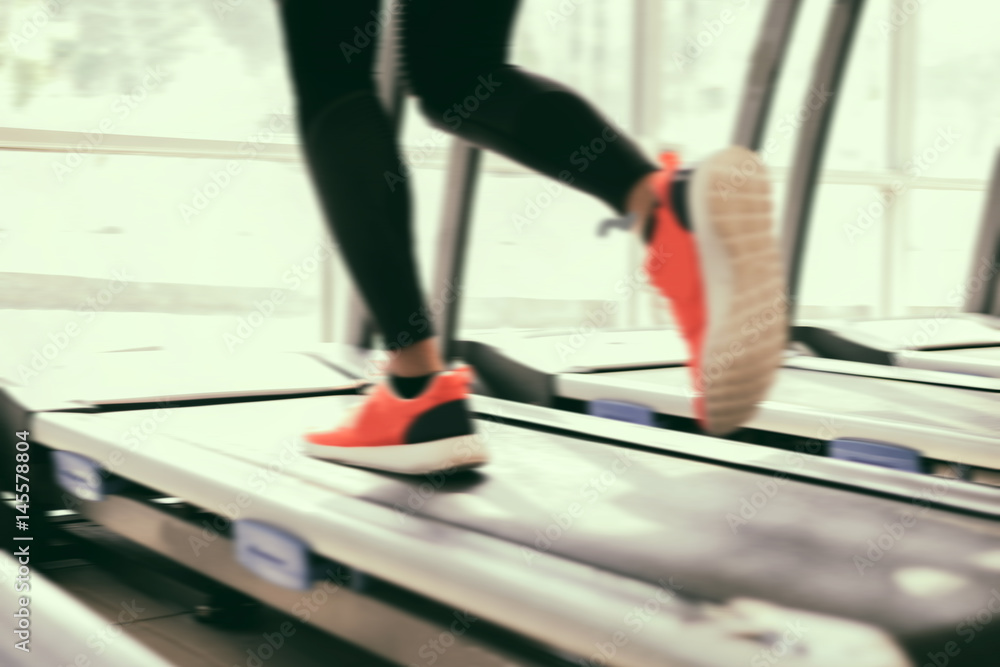 Blurry of running sport shoes at the gym while a young caucasian woman is having jogging on the treadmill Blurry of running sport shoes at the gym while a young caucasian woman is having jogging on the treadmill