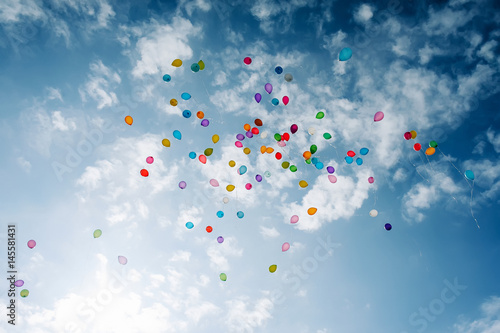 a lot of multicolored balloons in a blue sky with clouds.