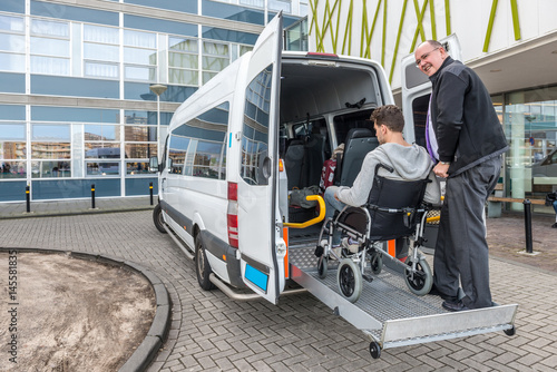 Driver Assisting Passenger In Wheelchair To Board Taxi photo