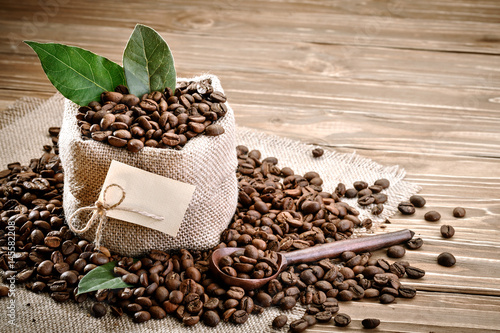 Bag of burlap filled with coffee beans on wooden background.