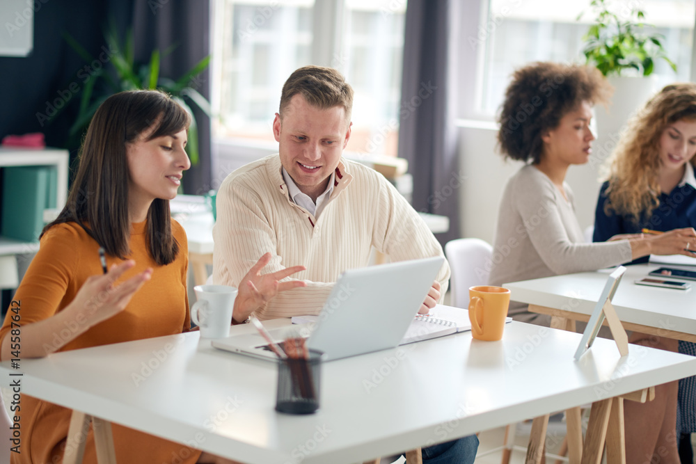 Young happy people discussing business standing at the whiteboard in modern light office, beautiful woman sitting at the table at forefront Young happy people discussing business standing at the whiteboard in modern light office, beautiful woman sitting at the table at forefront