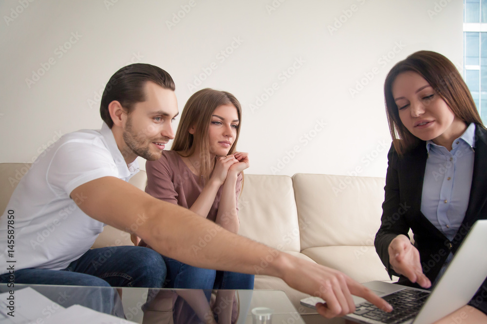 Cheerful couple visiting real estate or travel agency, sitting on sofa talking to female agent manager, looking at laptop screen, choosing resort, discussing property investment, planning wedding Cheerful couple visiting real estate or travel agency, sitting on sofa talking to female agent manager, looking at laptop screen, choosing resort, discussing property investment, planning wedding