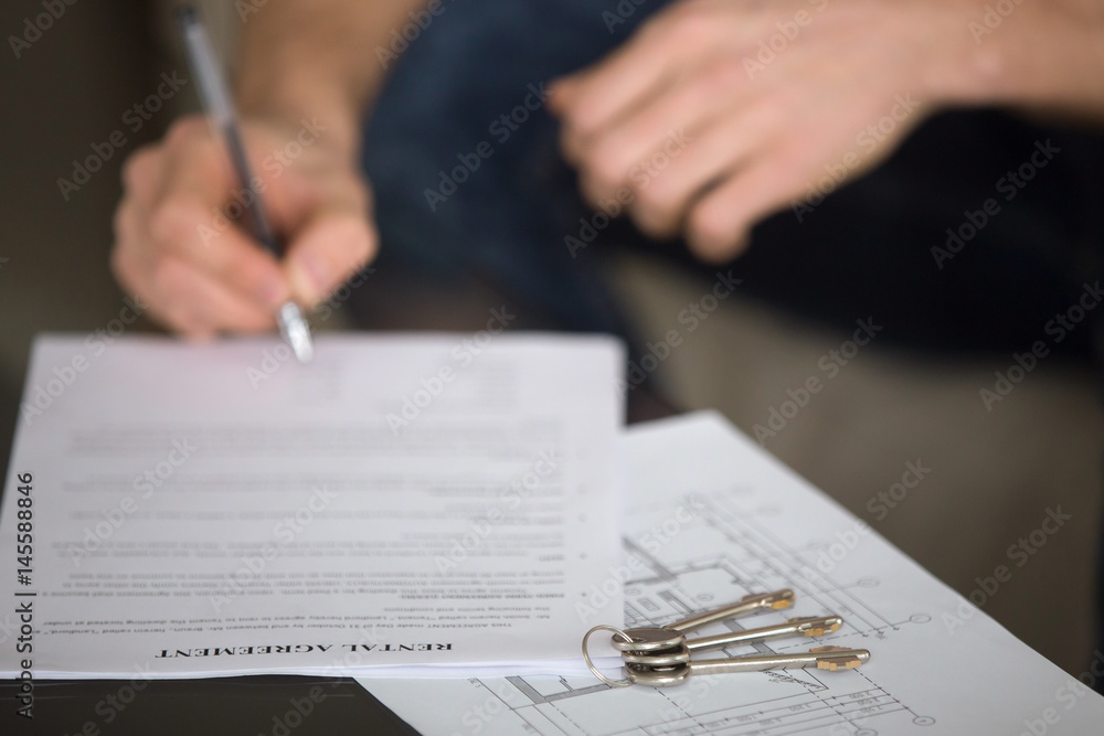 Close up of male tenant signing rental agreement, renter with a pen putting signature, focus on document and keys, young guy or student decided live separately and found home for rent Close up of male tenant signing rental agreement, renter with a pen putting signature, focus on document and keys, young guy or student decided live separately and found home for rent