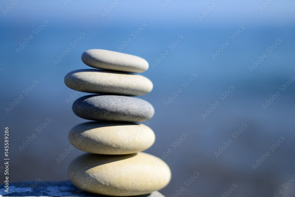 Fototapeta premium Zen spa stones with blue water and sky. Background with text space. Balance of stones. Sustainability, hierarchy and health life. Lifestyle tranquil.