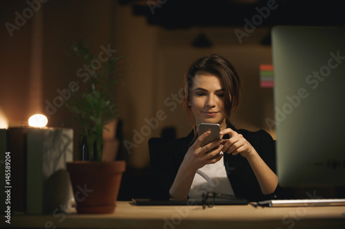 Pretty young woman designer sitting indoors chatting by phone