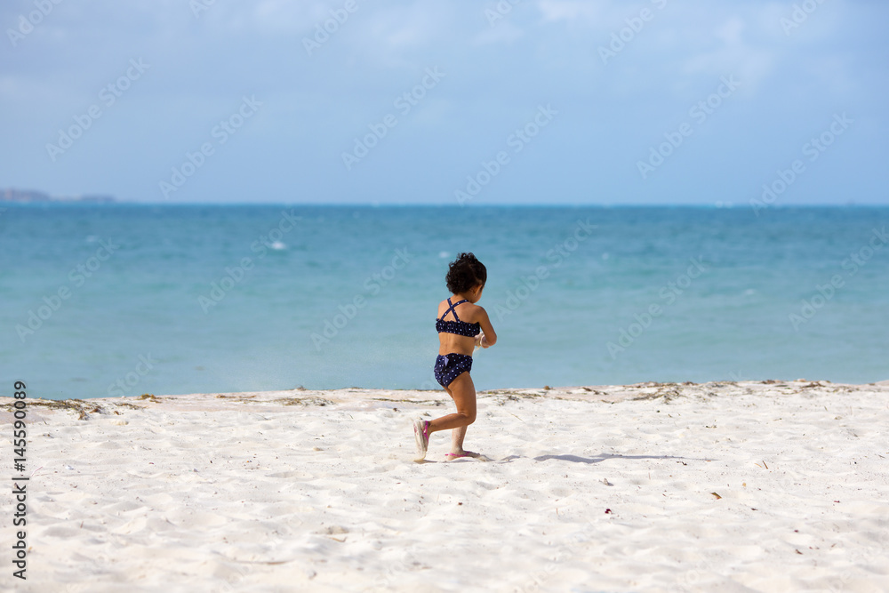 Child running on the beach. She is carrying sand while running.