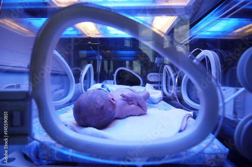 Newborn child baby having a treatment for jaundice under ultraviolet light in incubator. A neonatal intensive care unit (NICU), intensive care nursery (ICN) for premature newborn infants