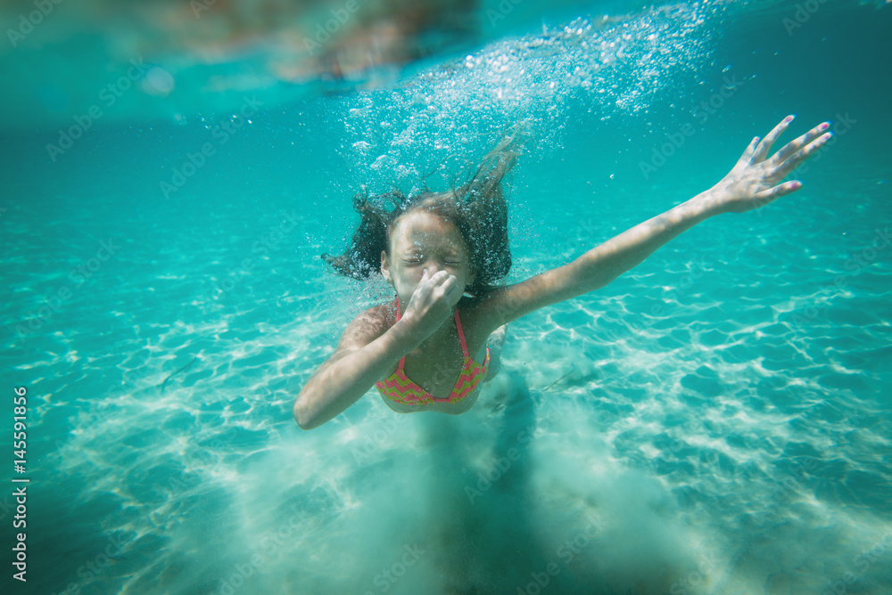 Beautiful little girl diving underwater in the sea. She is holding her nose with hand and