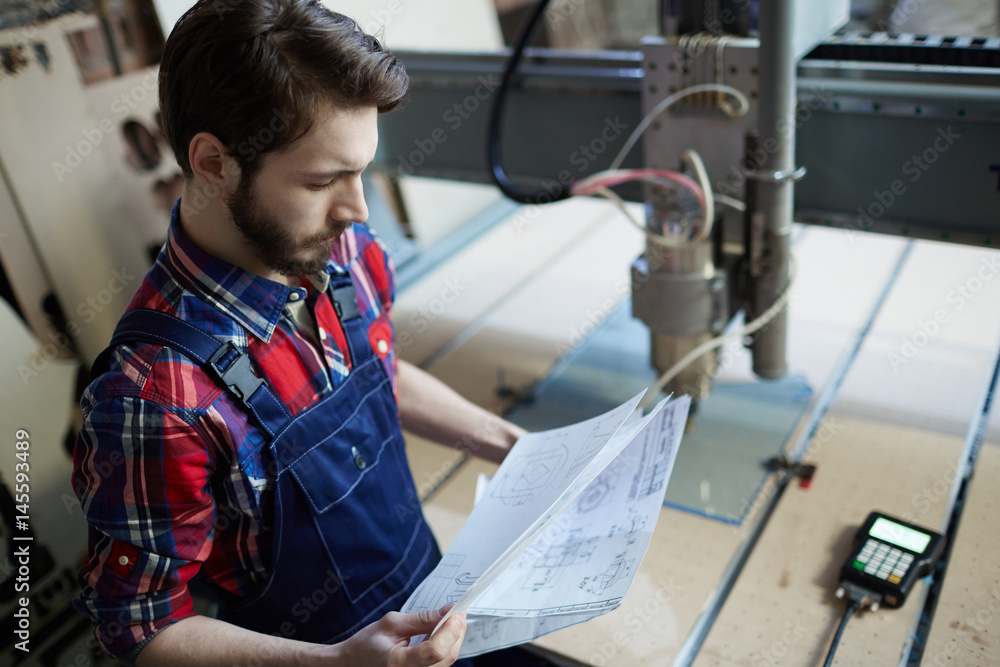 Obraz premium Serious engineer looking at technical sketches by workplace