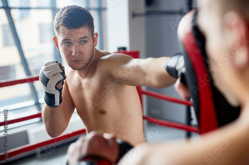 Portrait of handsome shirtless man practicing straight hitting focus mitts with partner in fighting club