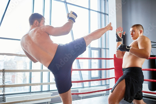 Portrait of shirtless wrestler fighting with opponent in boxing ring at fight practice: evading high kick in head photo