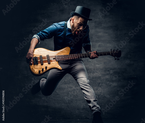 фотографія Funny bass player in a jump dressed in a cylinder hat.