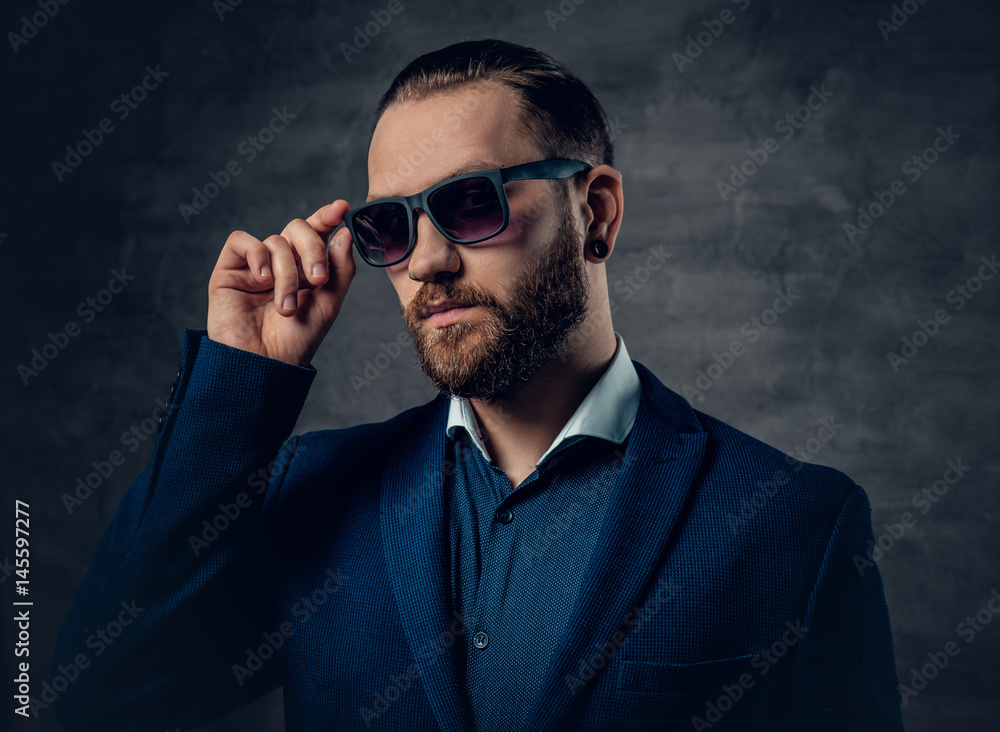 Stylish bearded male in sunglasses over dark grey background.