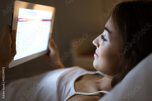 Beautiful young woman using her digital tablet in the bed at night.