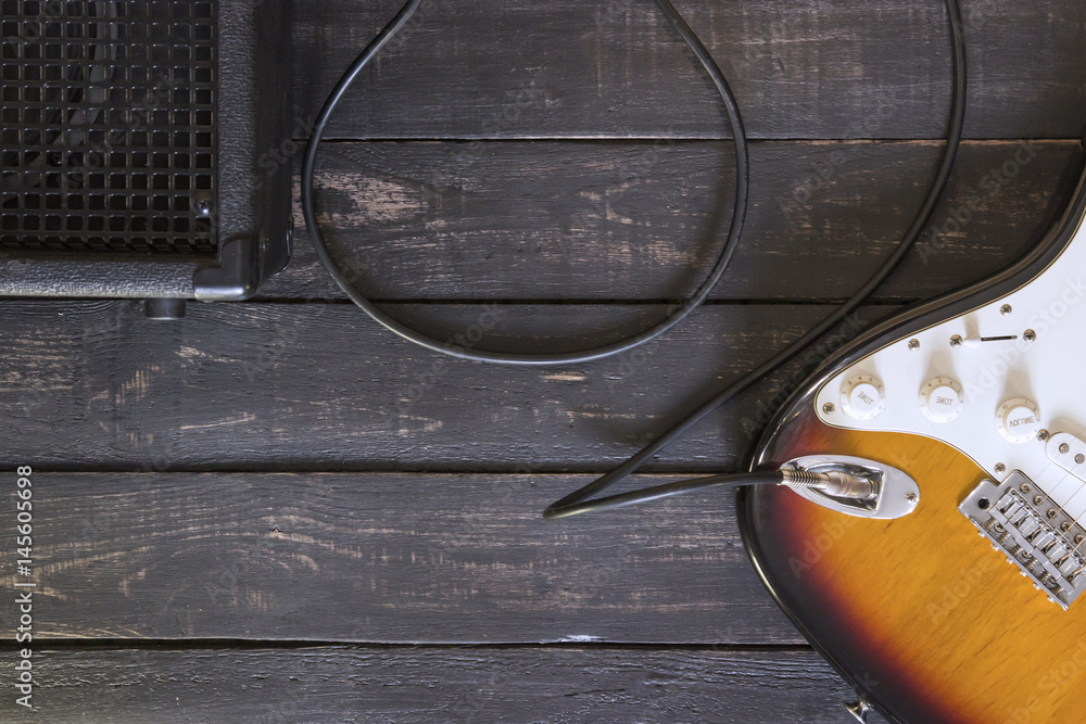Obraz premium Electric guitar and black amplifier connected by cable on wooden floor