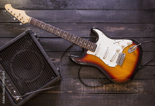 Electric guitar and amplifier connected by cable on wooden background