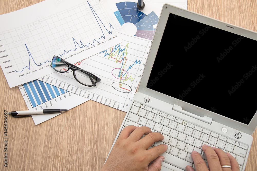 Man's hand typing on laptop computer. Business report, business summary laid on desk. Business work at home office Man's hand typing on laptop computer. Business report, business summary laid on desk. Business work at home office