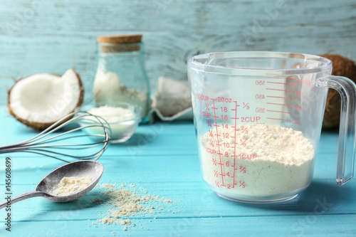 Measuring cup with coconut flour on wooden background
