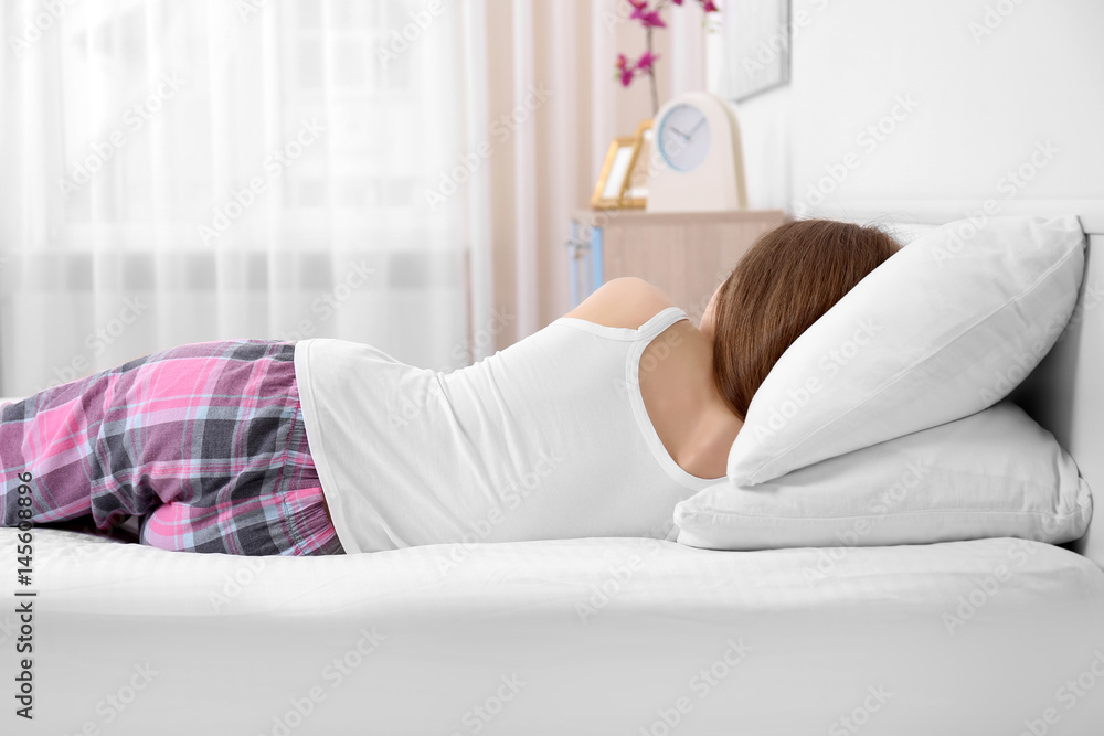 Young woman lying on bed with orthopedic pillow against blurred background. Healthy posture concept Young woman lying on bed with orthopedic pillow against blurred background. Healthy posture concept