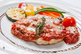 grilled Chicken breasts coated with melted cheese, vegetables and tomato sauce on a white plate
