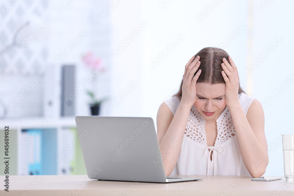 Beautiful young woman suffering from headache while sitting at table in office Beautiful young woman suffering from headache while sitting at table in office