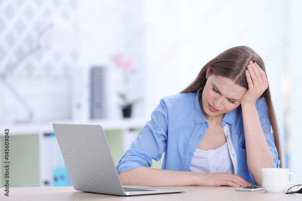 Beautiful young woman suffering from headache while sitting at table in office