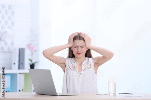 Beautiful young woman suffering from headache while sitting at table in office