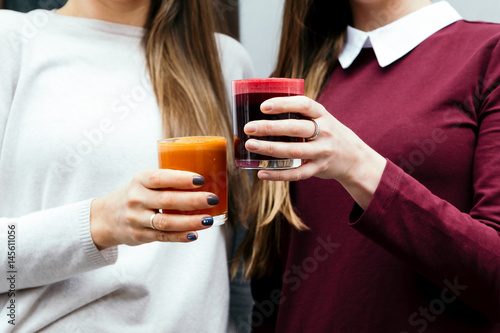 Close-up of two girl hands holding a glass of orange and beet juice, sitting in a cafe outdoors. dressed in white and burgundy clothes. Long hair photo