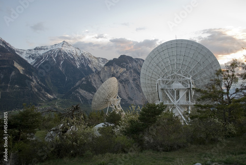 Landscape: series of radio telescope during sunset on the Swiss mountains, surrounded by colorful clouds and the moon on a spring day, Alps, Switzerland