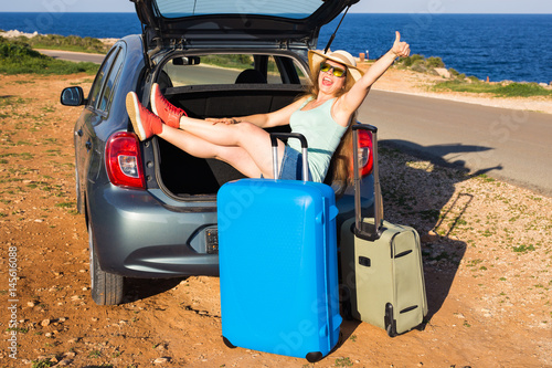 Travel, summer holidays and vacation concept - Young woman with suitcases on car trip. She is sitting in car back and gesture thumbs up.