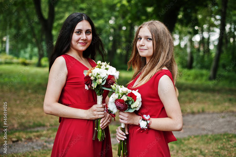 Two girls bridesmaids at red dresses with wedding bouquets.