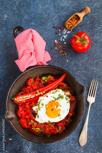 Mexican breakfast, Huevos Rancheros, chlli tomato stew and fried eggs on a black cast-iron skillet on dark concrete background, top view. photo