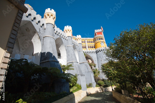 View of the Pena Palace. View from the park. The castle is on top. Tall trees
