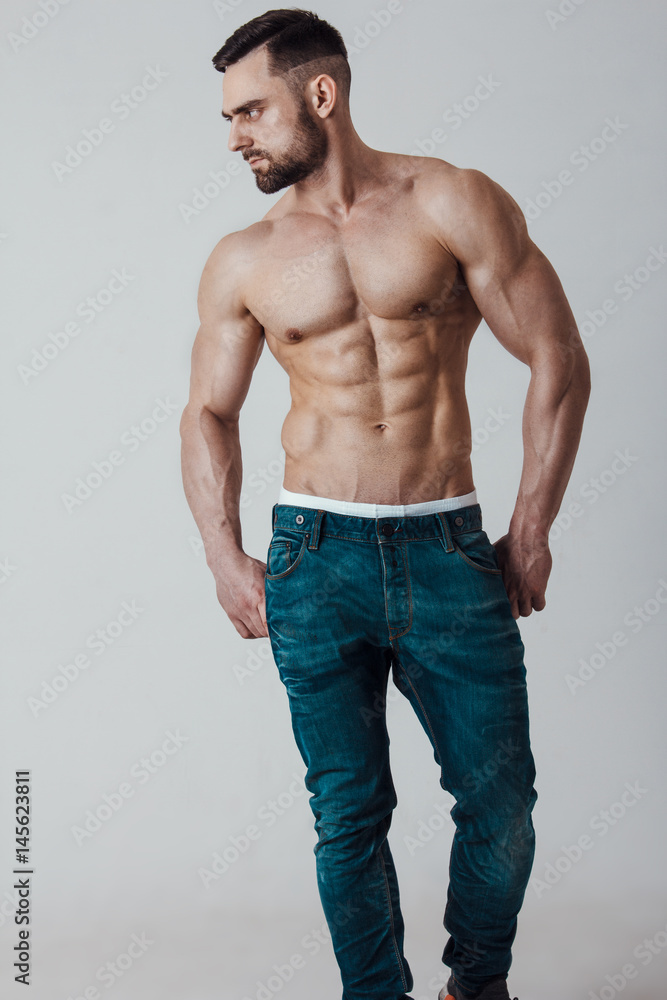 Muscle male model with muscular body in jeans posing on grey background. Studio shoot. Muscle male model with muscular body in jeans posing on grey background. Studio shoot.