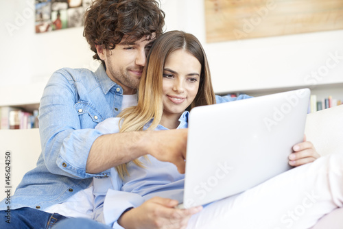 Spend time together. Shot of a smiling young woman and an affectionate handsome man relaxing at home and using laptop. 