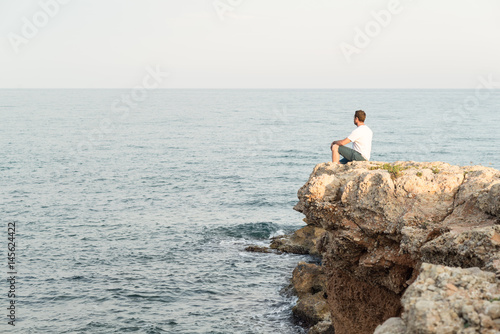 Hombre joven sentado al borde de un acantilado al atardecer. Mar Mediterráneo